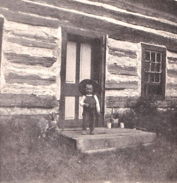 Jack MacQuarrie poses in front of his grandparents' log house, ca. 1918. Photo courtesy of the McQuarrie family.