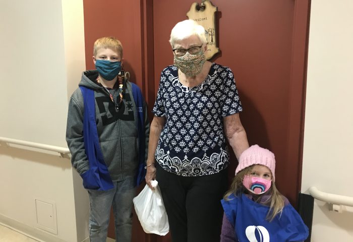 Two children posing with a woman as they deliver her a card