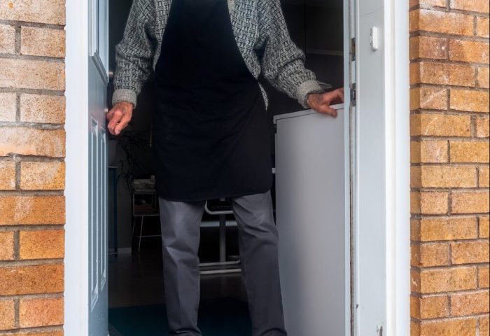 Elderly man standing in his doorway, with a package of food on his doorstep